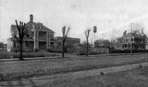 Historic photograph of two large houses along a tree-lined street, showcasing early 20th-century architecture.