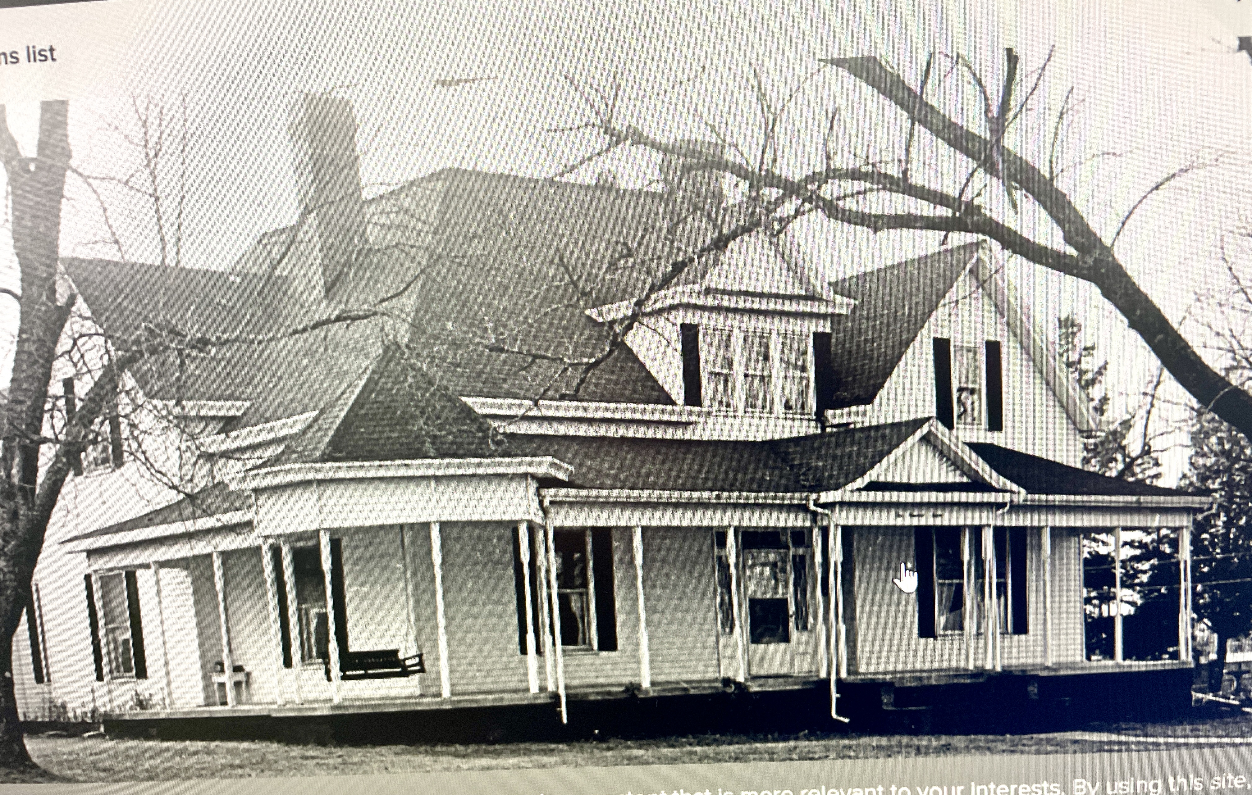Black and white historical photo of the Magnolia Inn, built in 1895. The image shows the inn's charming Victorian-style architecture, featuring a wraparound porch, large windows, and a swing on the porch. Bare trees surround the building, highlighting its classic design