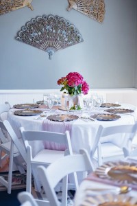 Elegant table setting with white chairs, a centerpiece of pink hydrangeas, and decorative wall fans, creating a festive and serene atmosphere.