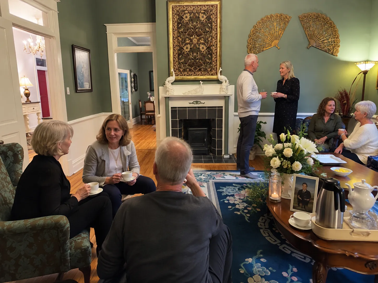 Guests sharing tea and conversation during a community gathering in a historic parlor.