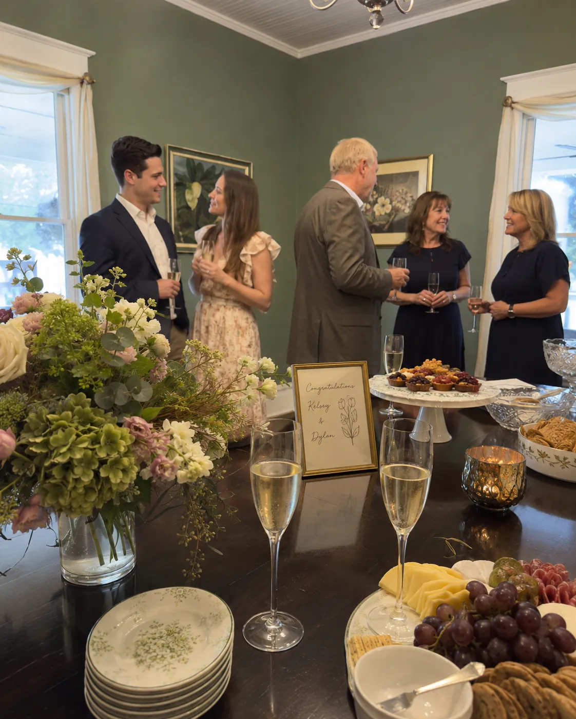 Guests celebrating an engagement with champagne, flowers, and appetizers in a historic dining room.