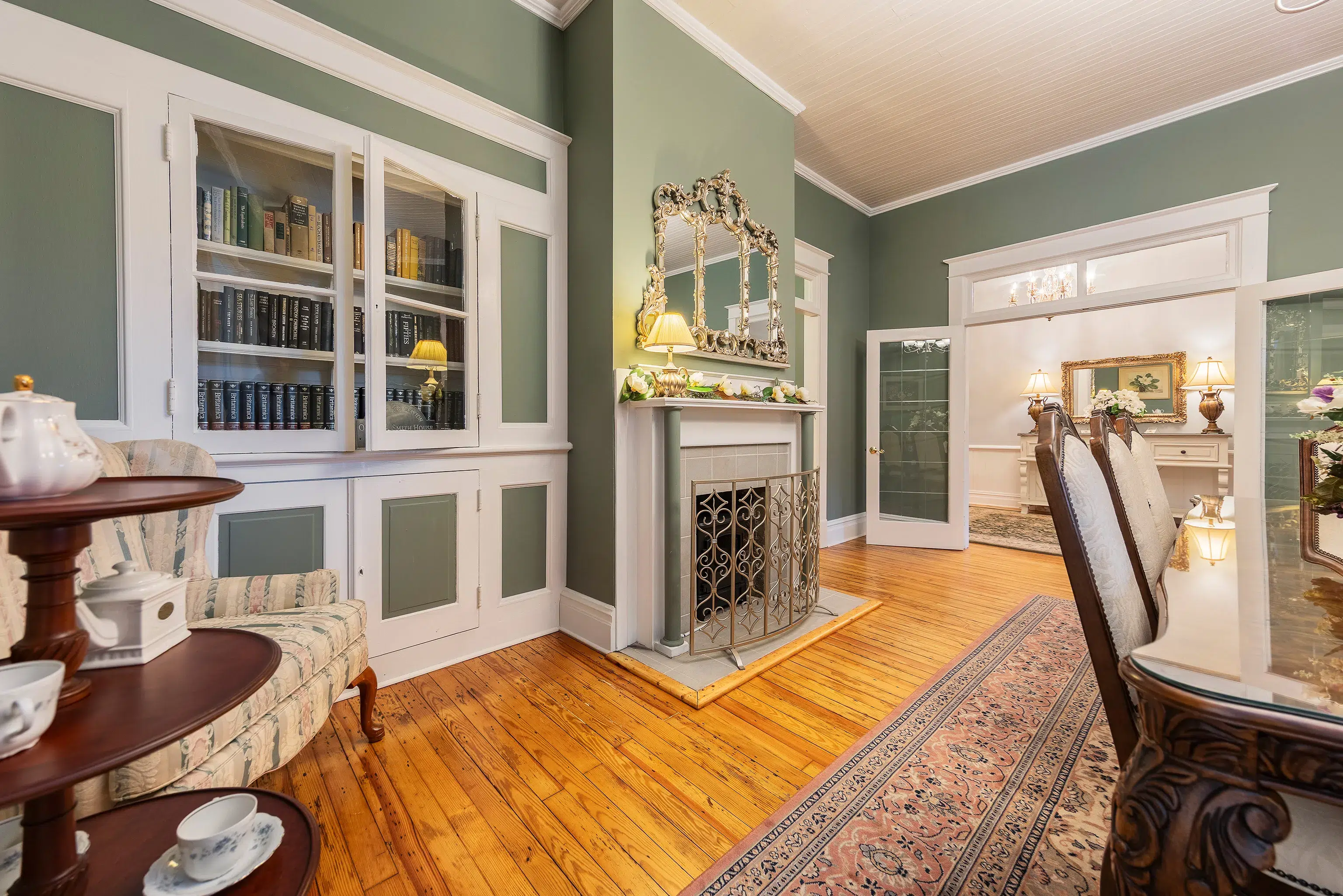 Historic dining room with sage green walls, a built-in bookcase, fireplace, and tea service.