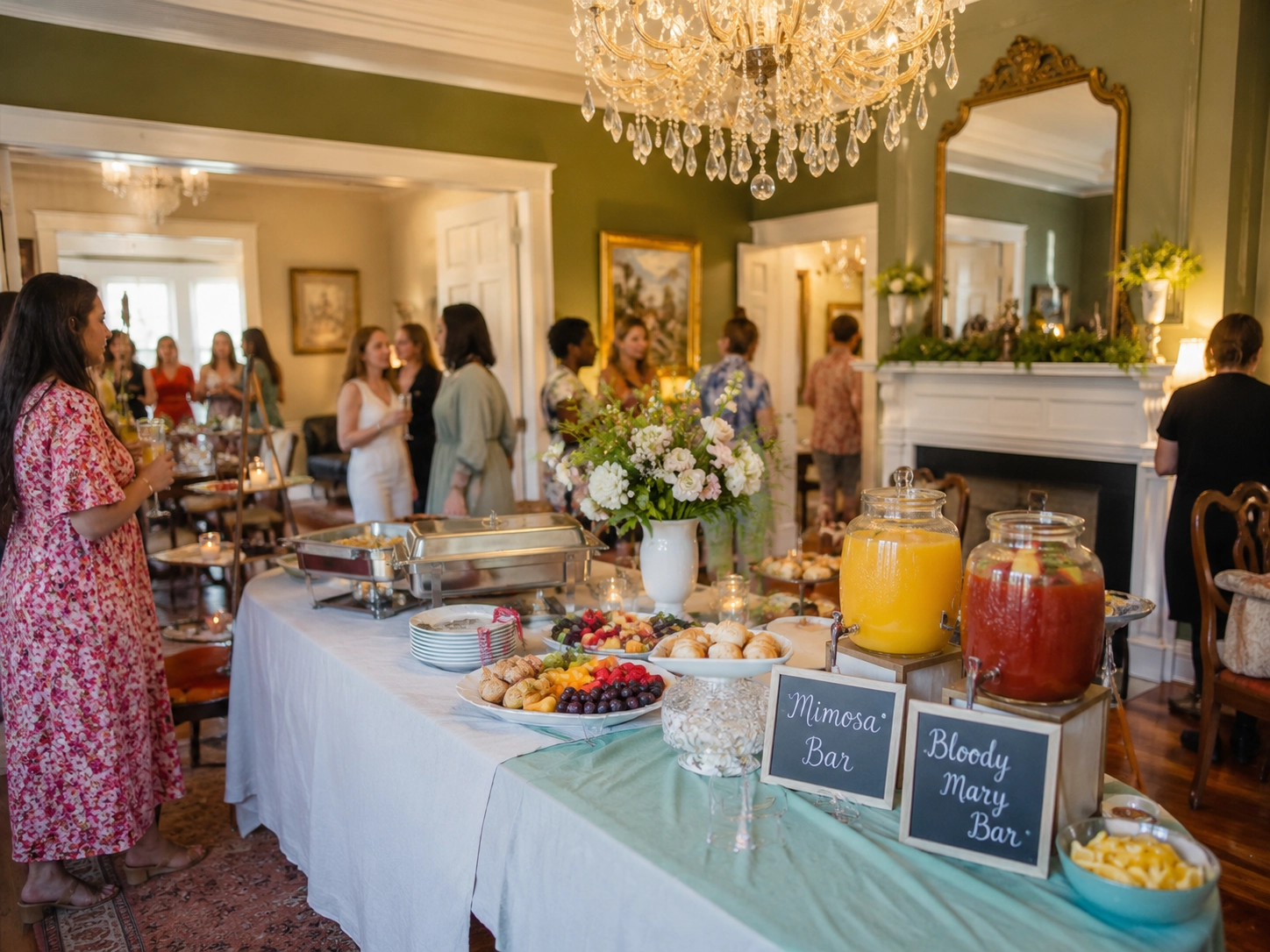 A bright, elegant brunch gathering with a buffet table featuring fruit, pastries, and juice labeled Mimosa and Bloody Mary bars. Guests chat in a cozy room.