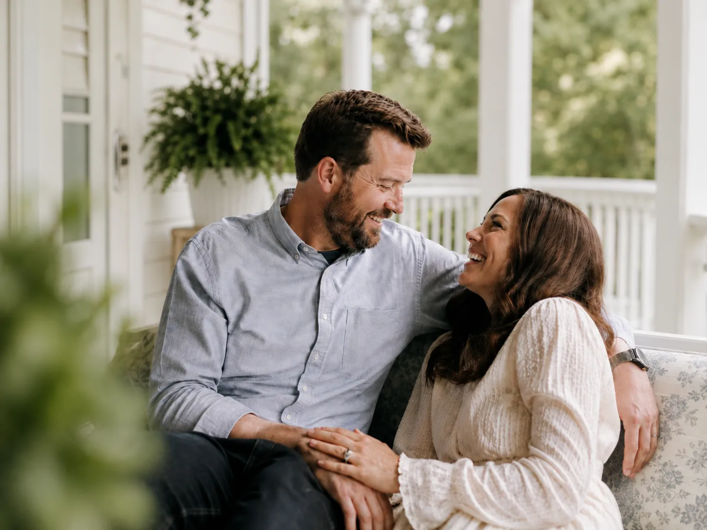Engaged couple smiling together at the base of a grand staircase in a historic inn.